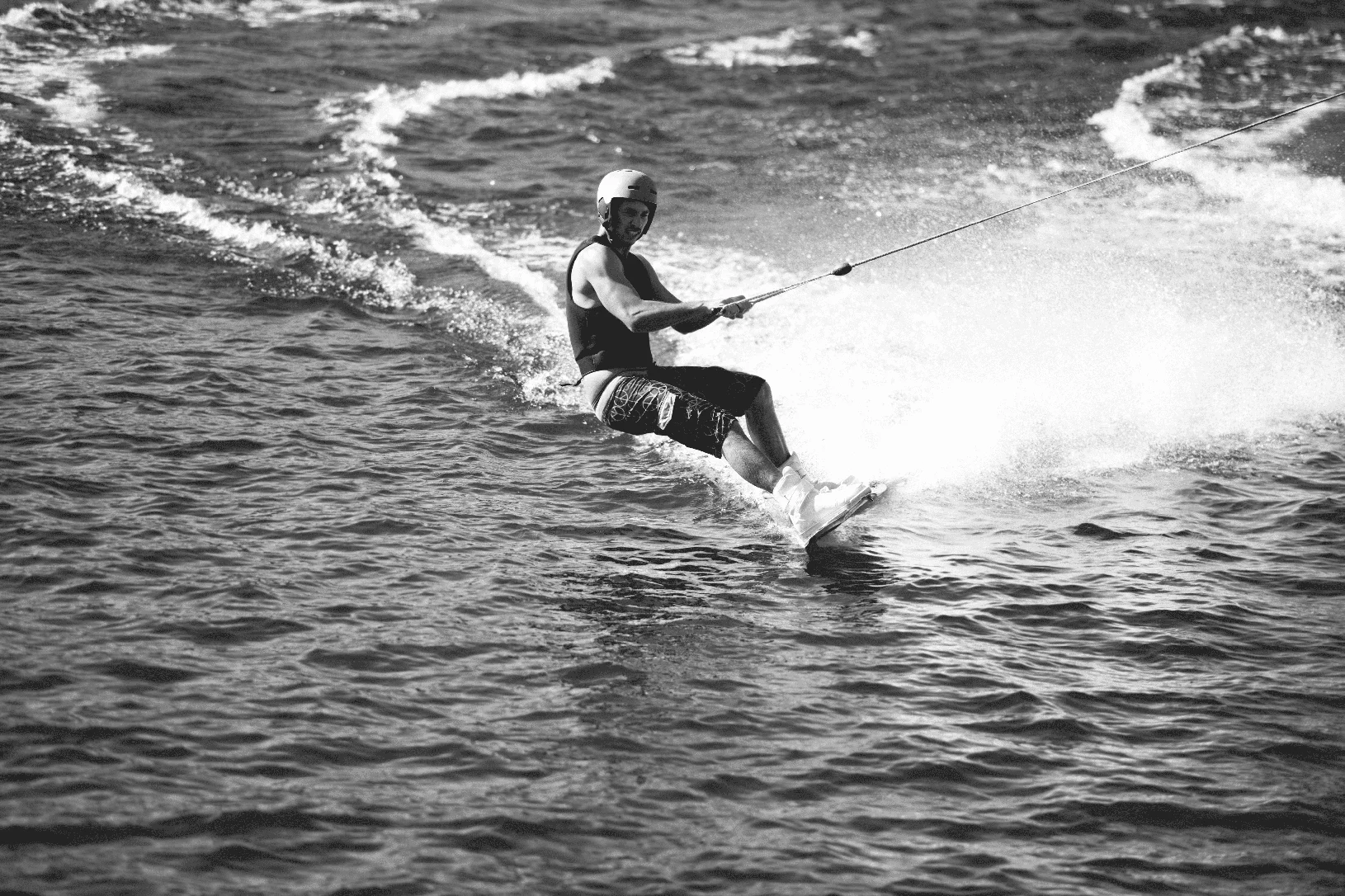 Un jeune homme portant un casque et un gilet de sauvetage faisant du wakeboard sur un lac